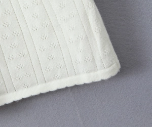 Vue détaillée en gros plan du tissu tricoté blanc cassé avec motifs floraux ajourés et rayures