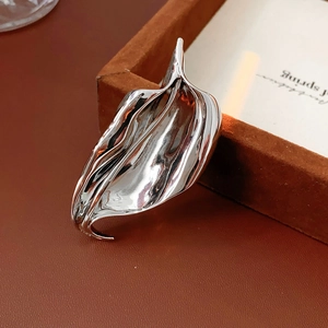Detailed close-up of a polished silver irregular leaf brooch on a premium leather base