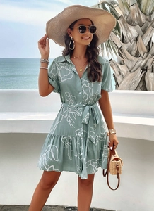 Elegant light green geometric print dress styled with a straw hat and bag by the sea
