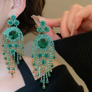 Macro shot of elegant gold fringe earrings with large emerald green crystals and diamonds