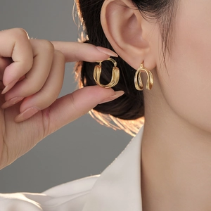 Detailansicht dreilagiger goldener geometrischer Ohrringe für elegante Textur am Ohr