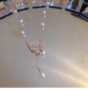 Detailed view of a gold-plated butterfly necklace with freshwater pearls on a mirror