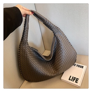 Detail shot of a dark grey woven handbag held against a soft neutral background