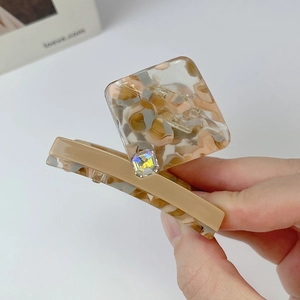 Close-up of acetic acid hair claw with square marble pattern and rhinestone detail