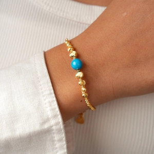 Close-up of gold beaded necklace featuring blue turquoise stone and heart charm