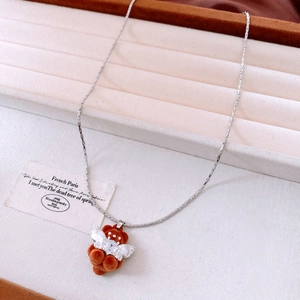 Detail of a brown flocked bear necklace with zircon wings on a beige jewelry display tray