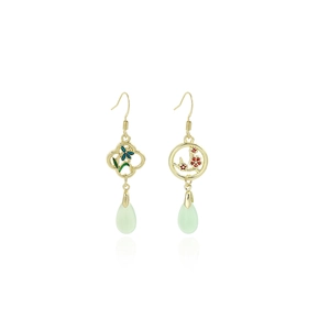 Detail of asymmetric gold earrings with blue and red floral patterns and green teardrops