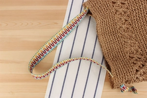 Macro view of woven straw beach bag featuring hollow floral crochet and a colorful strap