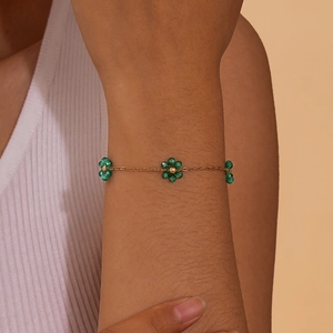 Elegant gold flat cross chain bracelet with green emerald bead flowers on woman's wrist