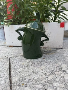 Detail of dark green ceramic canister with attitude, featuring lid and side handles