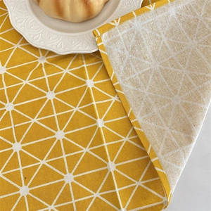 Detail of yellow cotton linen placemat with white geometric patterns and stitched edges