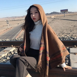 Brown hooded poncho with colorful stripes and tassels worn by a model in a desert setting