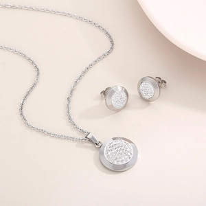 Detailed view of silver circular crystal necklace and stud earrings set on a beige surface
