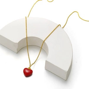 Detailed macro view of a glossy red heart pendant with a polished golden bead chain