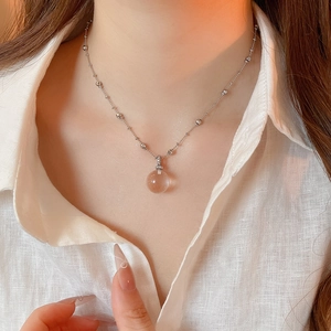 Close-up of minimalist crystal sphere pendant necklace with silver beaded chain on model