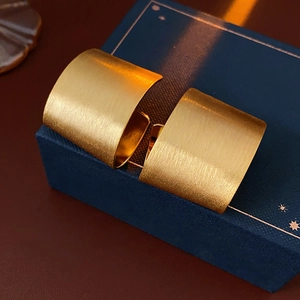 Detail of wide C-shaped gold-plated earrings with a brushed matte texture on jewelry box