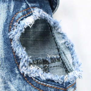 Macro shot of denim pet vest showing vintage distressed holes and contrast orange stitching