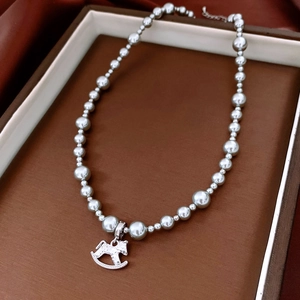 Macro detail of a silver rocking horse pendant on a pearl necklace in a display box