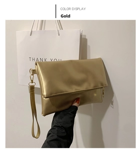 Primer plano de un bolso de mano tipo sobre dorado metalizado con asa y cremallera