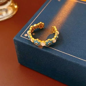 Detailed close-up of 18k gold-plated ring with blue enamel flowers and white beads