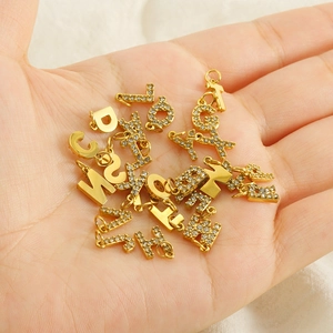Detailed view of gold alphabet charms with tiny diamonds held in palm for scale