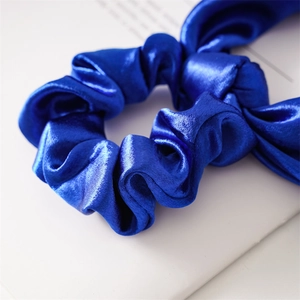 Close-up of royal blue satin scrunchie with smooth silk texture and soft fabric folds