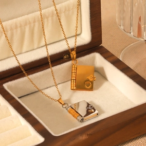 Macro detail of heart-shaped book pendants in gold and two-tone steel inside a wooden box