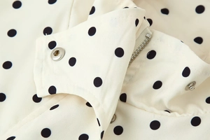 Detailed close-up of metallic zipper and snap button on polka dot print jacket