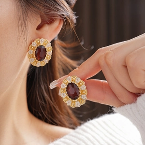 Close-up of vintage gold stud earrings with a deep red oval gem and white flower details