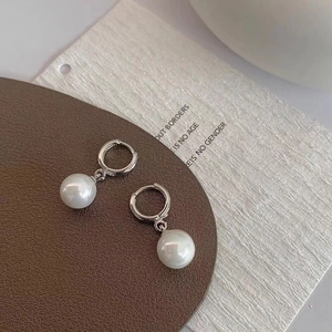 Elegant French style pearl drop earrings with silver metal hooks on a textured background
