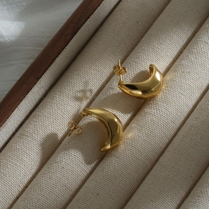 Polished gold crescent stud earrings made of stainless steel displayed in a jewelry box