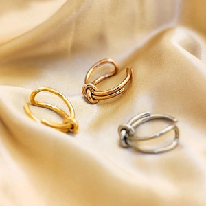 Close-up of knot design rings in gold, rose gold and silver on champagne silk fabric