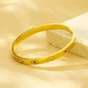 Detail of gold evil eye bangle with blue and white crystals on textured stone background