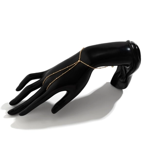 Detail of gold chain finger bracelet with beads on a black mannequin hand