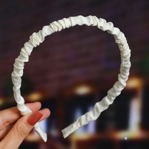 Detailed view of a white pleated satin headband featuring a wavy texture and smooth finish