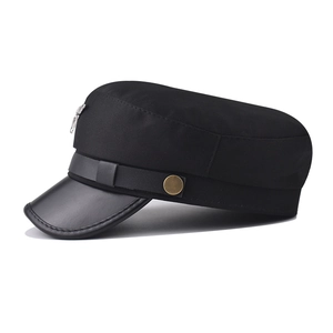 Detail of black military cap featuring leather brim and metallic bird emblem ornament