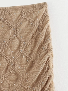 Gros plan sur tissu dentelle beige avec motifs tricotés et détails de paillettes brillantes