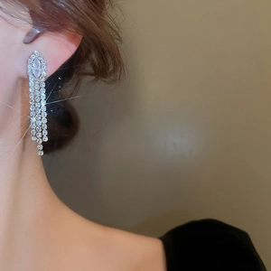 Macro detail of elegant silver tassel earrings with zircon stones worn by a model