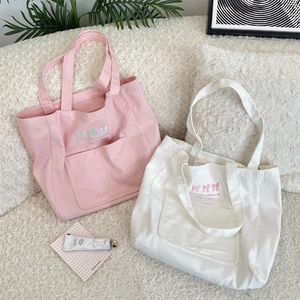 Détail des nœuds brodés et de la poche externe sur les sacs cabas en toile rose et blanc