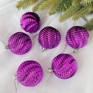 Detail von lila Weihnachtskugeln mit Wellentextur und silbernen Schlaufen auf Tannenzweigen