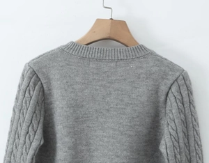 Detail of grey cable-knit sweater showing ribbed crew neck and textured shoulder patterns