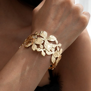 Close-up of gold hollow flower cuff bracelet on wrist featuring intricate floral relief