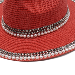 Macro detail of red straw fedora hat featuring rhinestone and pearl embellishments