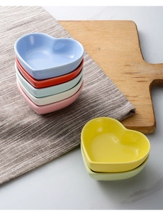 Top view of seven colorful heart-shaped ceramic sauce dishes on a rustic linen background