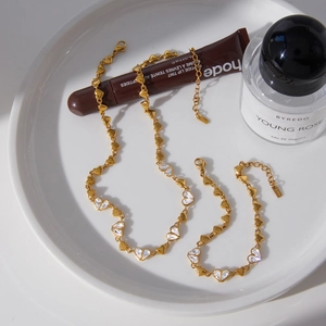 Ensemble collier et bracelet dorés à motifs de cœurs et cristaux sur coupelle