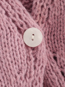 Detailed macro view of pink chunky knit fabric with a white round two-hole button