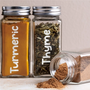 Macro shot of glass spice jars with silver lids and white labels on a beige background