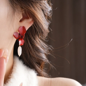 Close-up of red floral earrings with pearl drops worn by a model in soft lighting