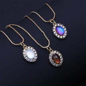 Drie gouden kettingen met ovale kristallen hangers in wit, blauw en zwart op donkere basis