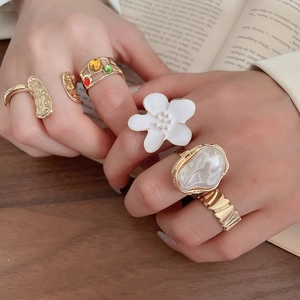 Close-up of gold flower rings and pearl bands worn over an open vintage book background